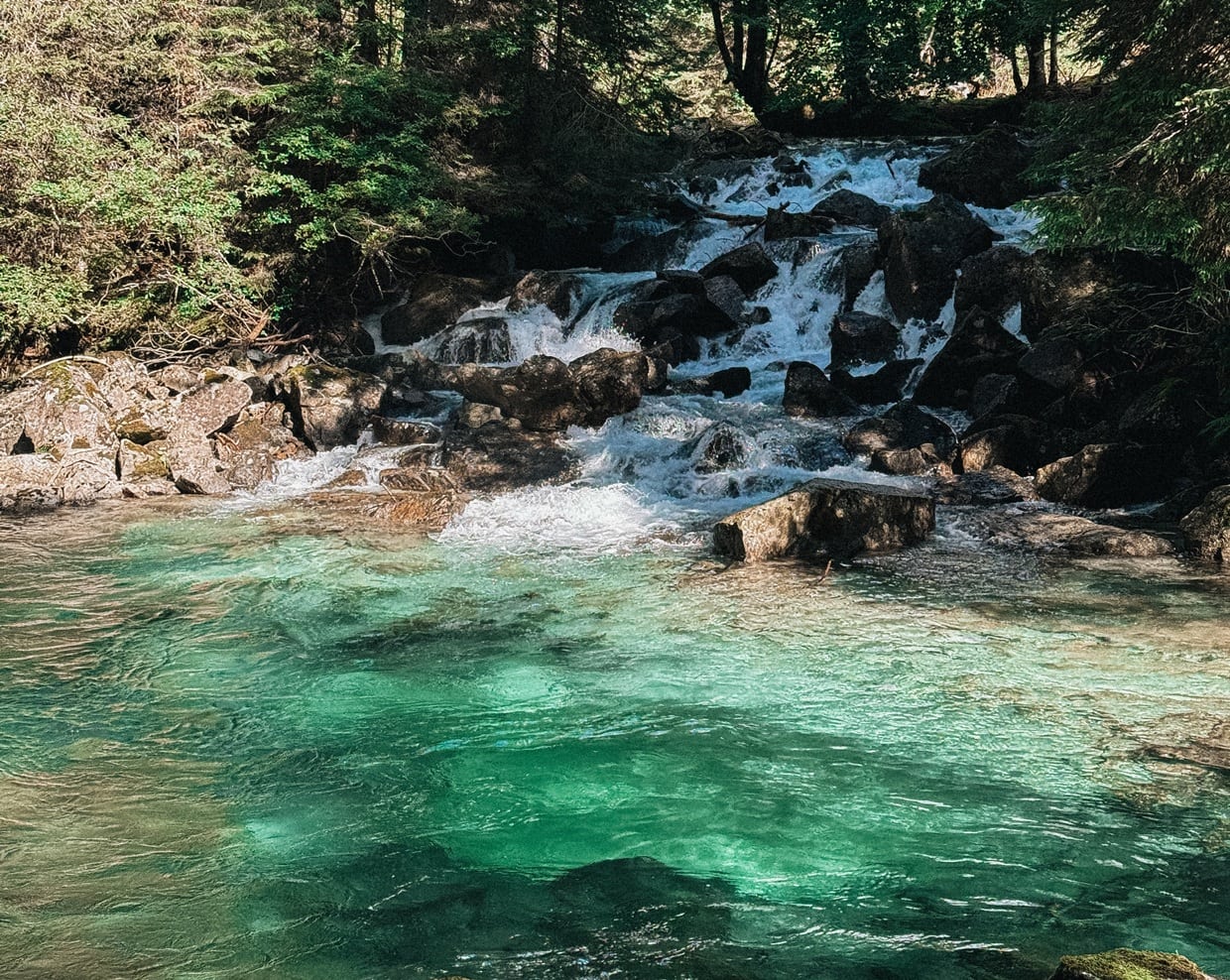 Cascata su rocce con acqua turchese che scorre, circondata da alberi e vegetazione