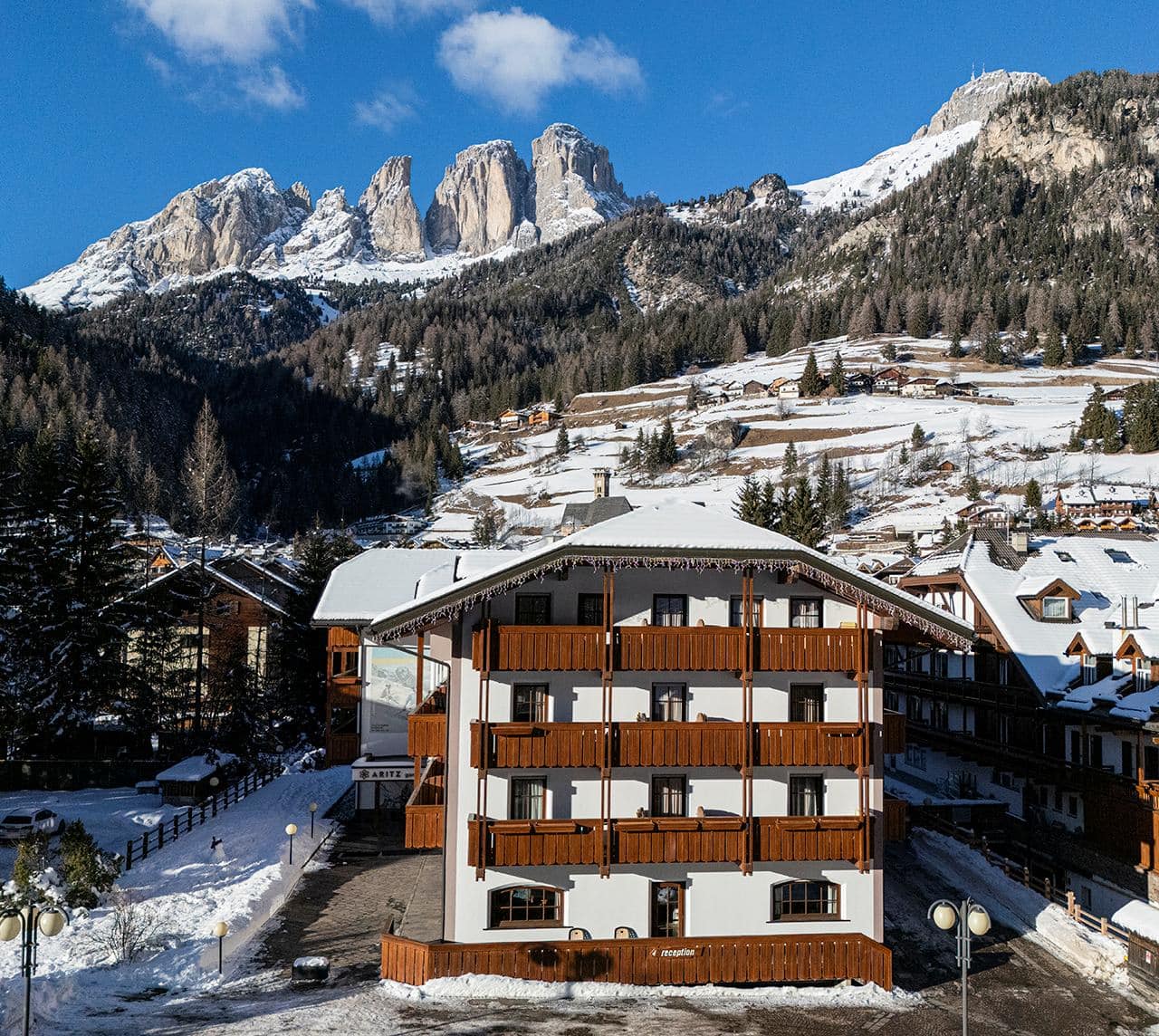 Edificio alberghiero alpino con balconi in legno e fiori, davanti a boschi e alte cime rocciose