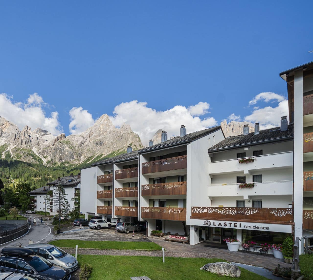 Edificio Lastei residence con balconi in legno, parcheggio e montagne rocciose sullo sfondo