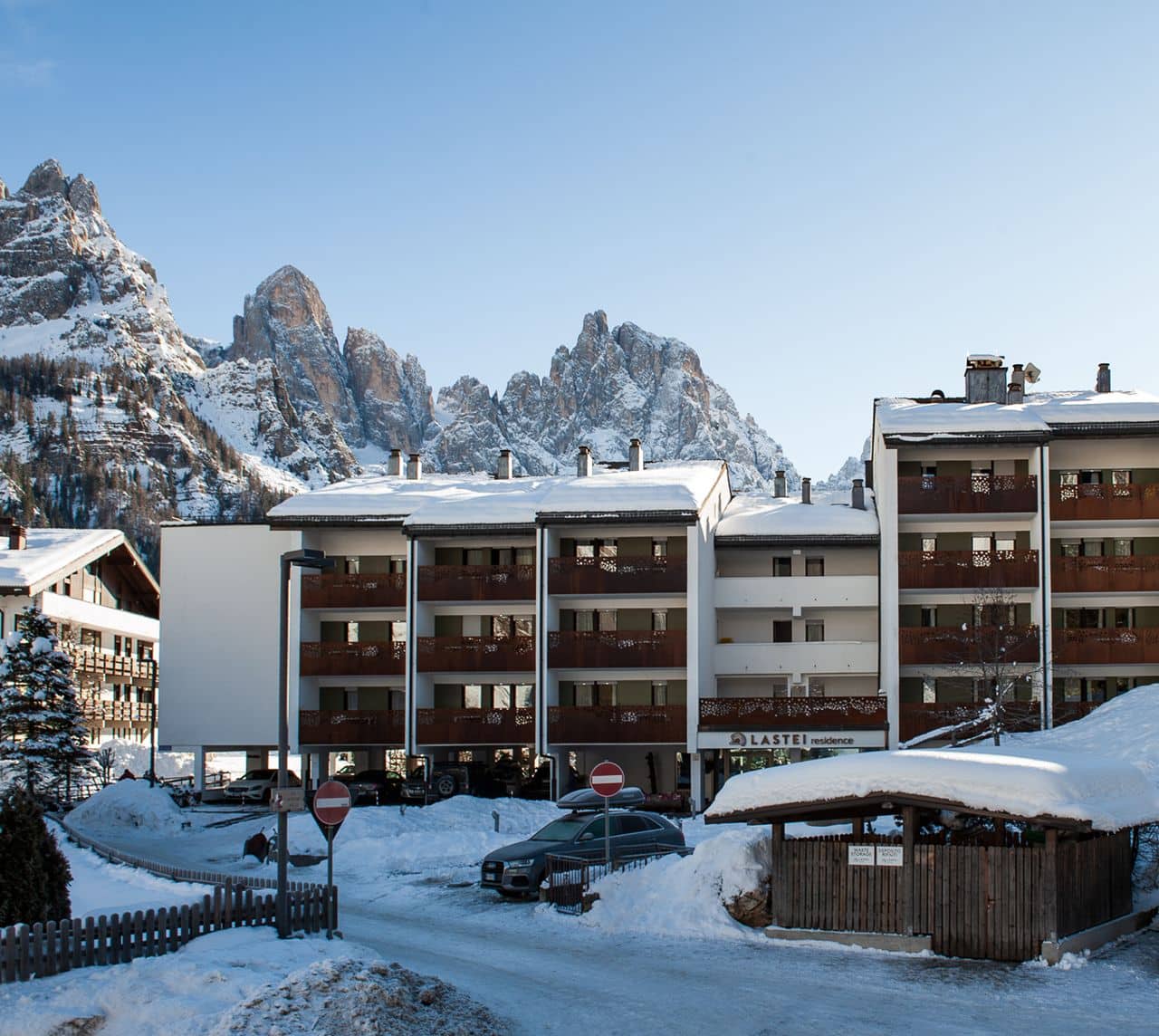 Edificio Lastei residence con balconi in legno, parcheggio e montagne rocciose sullo sfondo