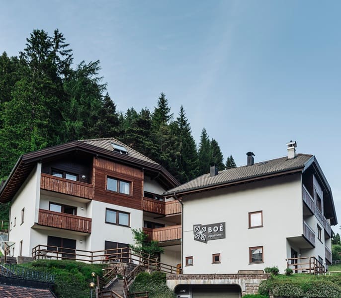 Complesso BOÈ Apartments su pendio con balconi in legno e bosco sullo sfondo