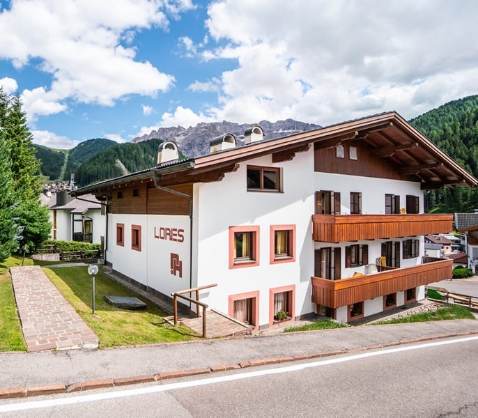 Edificio Lores a tre piani con balconi in legno su strada, montagne boscose sullo sfondo