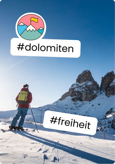 Person auf Skiern mit grünem Rucksack blickt auf schneebedeckte Felsgipfel; Text: #dolomiten #freiheit