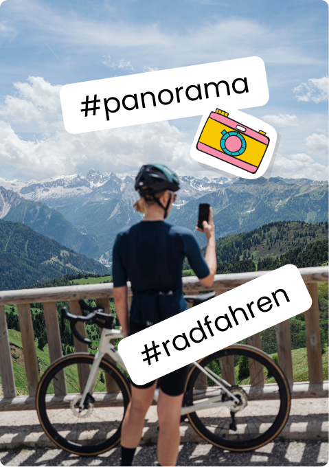 Person mit Rennrad fotografiert Bergpanorama an Holzgeländer.