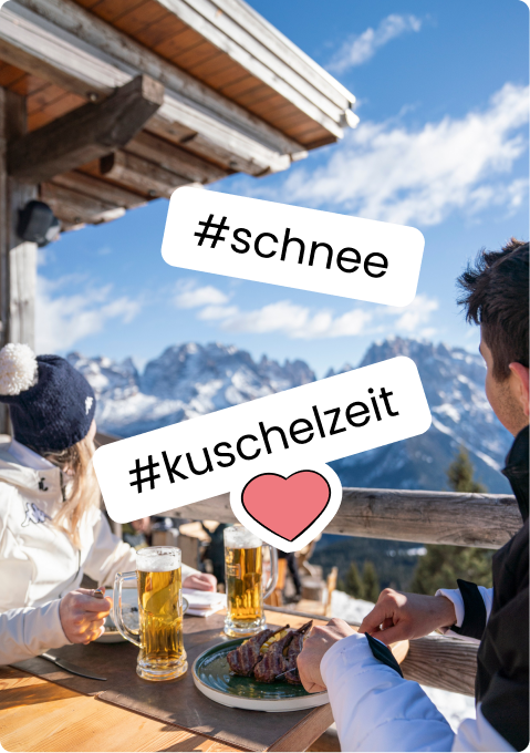 Zwei Personen an Berghütte sitzen mit Bier und Essen, verschneite Gipfel im Hintergrund, '#schnee' '#kuschelzeit'