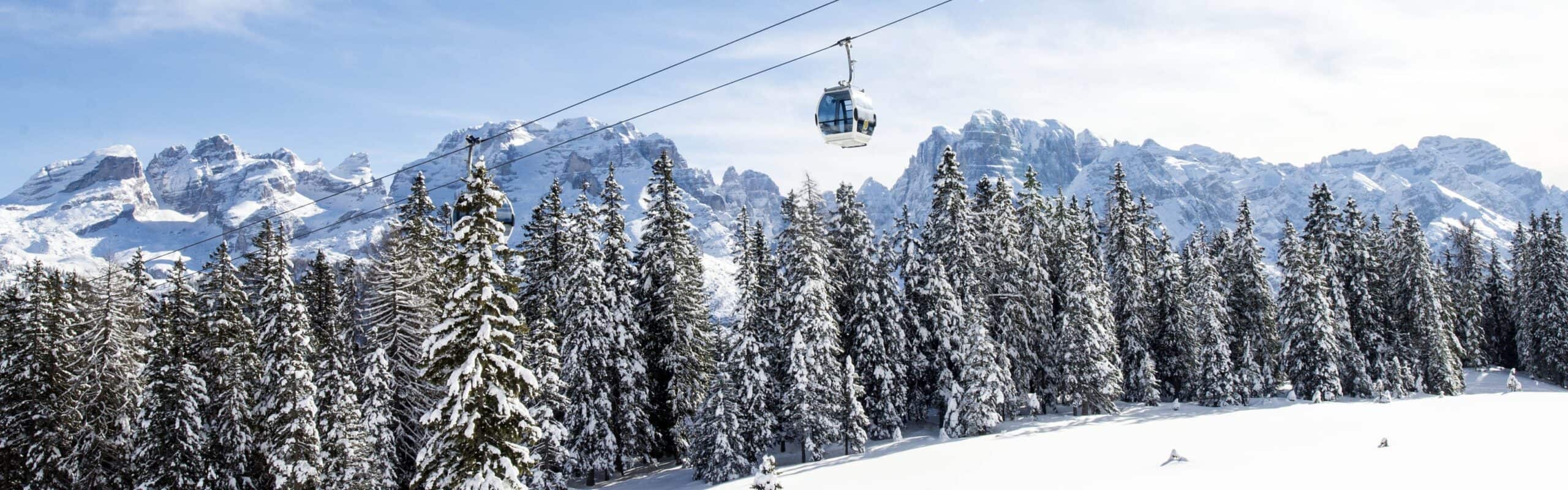 Cabina della funivia sospesa sopra una foresta di conifere innevate, montagne innevate sullo sfondo