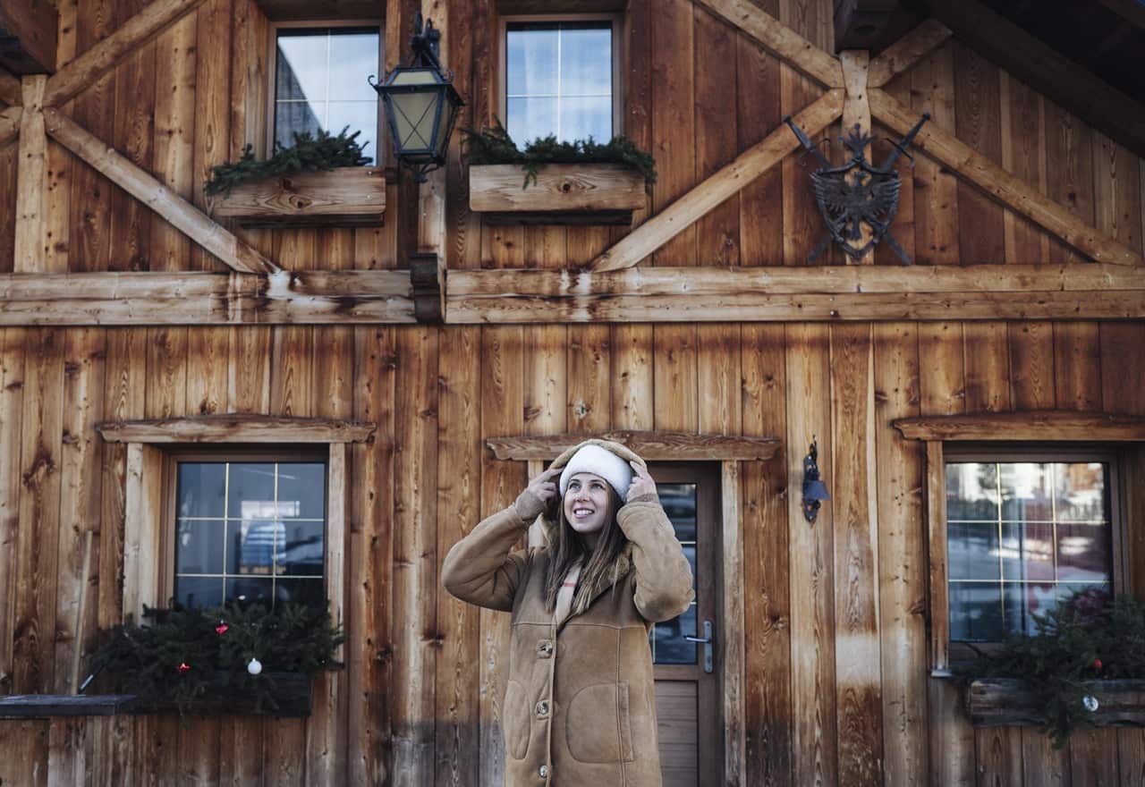 Donna con cappotto che si sistema il berretto davanti alla facciata di uno chalet in legno