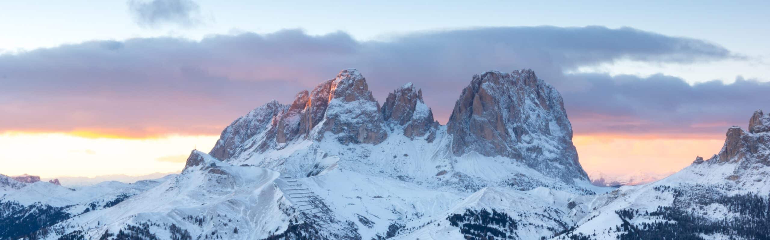 Massiccio roccioso innevato al tramonto con creste e vallate innevate sotto un cielo arancione e nuvoloso