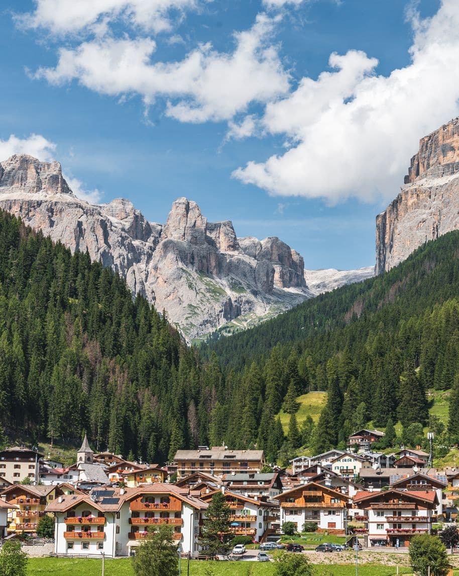 Paese alpino ai piedi di una foresta con pareti rocciose sullo sfondo.