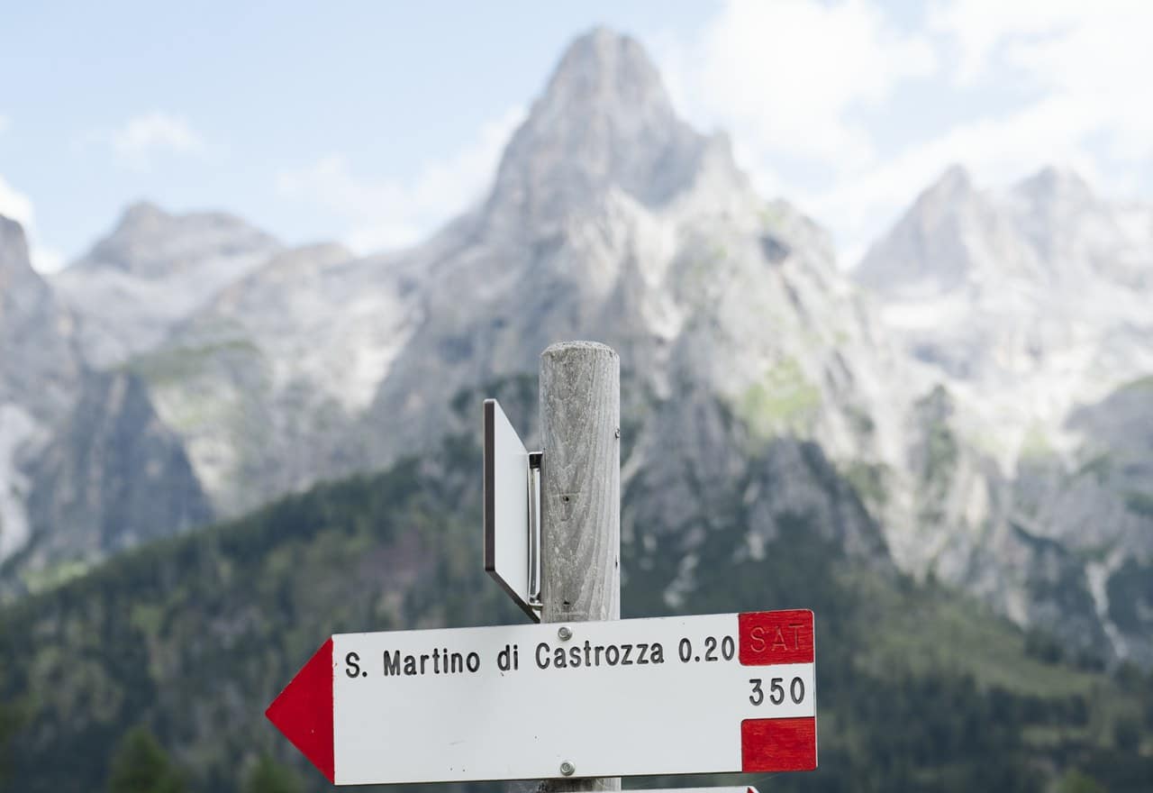 Palina in legno con freccia S. Martino di Castrozza 0.20, montagne rocciose sullo sfondo