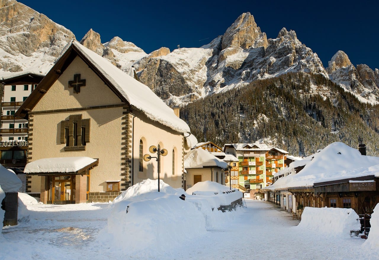 Chiesa con tetto innevato in un paese alpino, case e montagne rocciose sullo sfondo