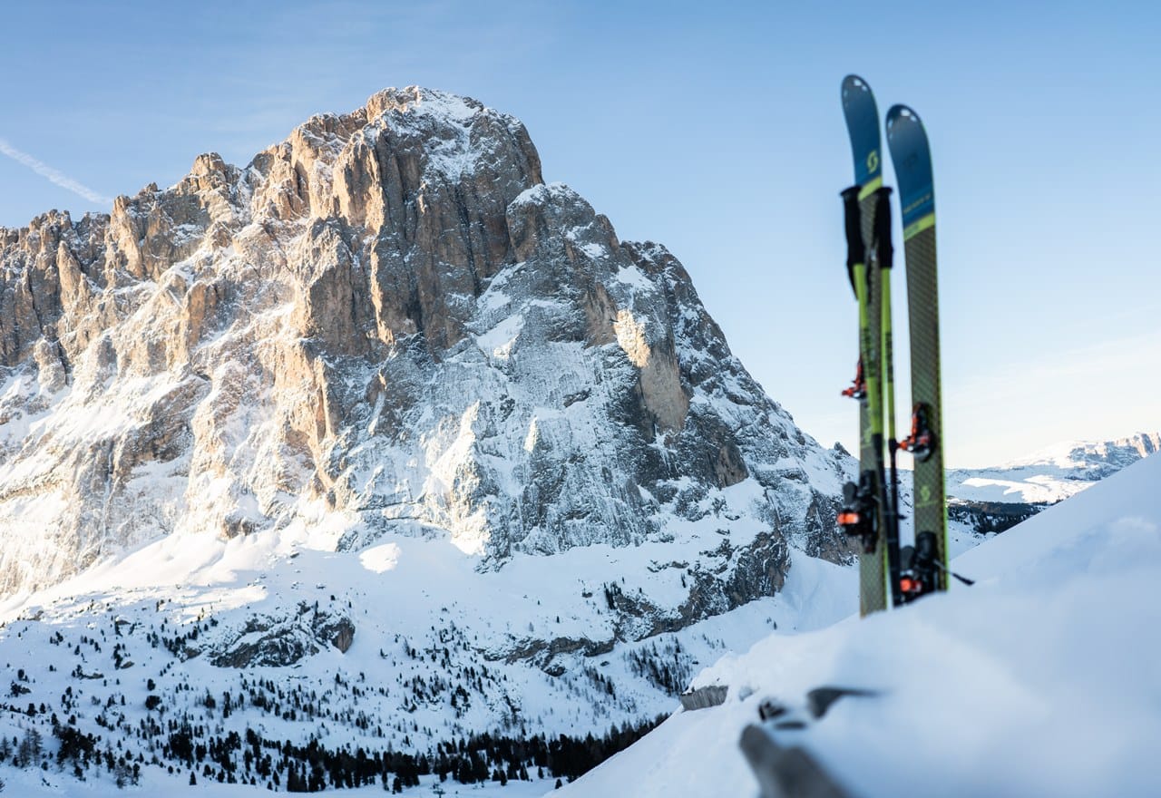 Due sci verticali appoggiati nella neve in primo piano; parete rocciosa innevata sullo sfondo