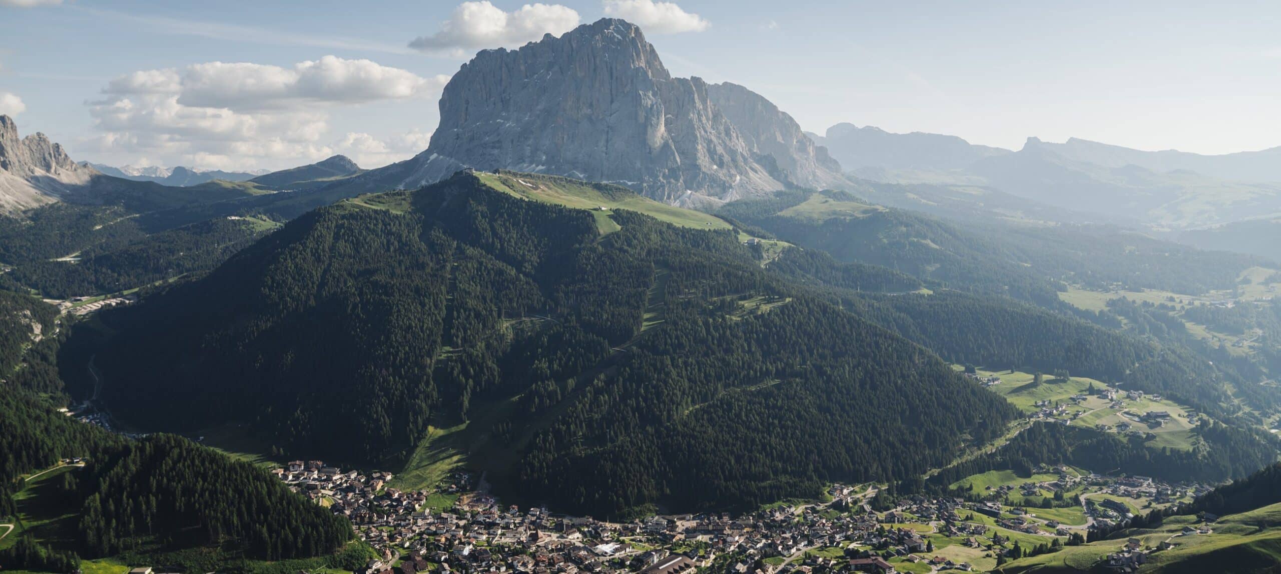 Massiccio roccioso che domina colline boschive e un paese nella valle, cielo con poche nuvole