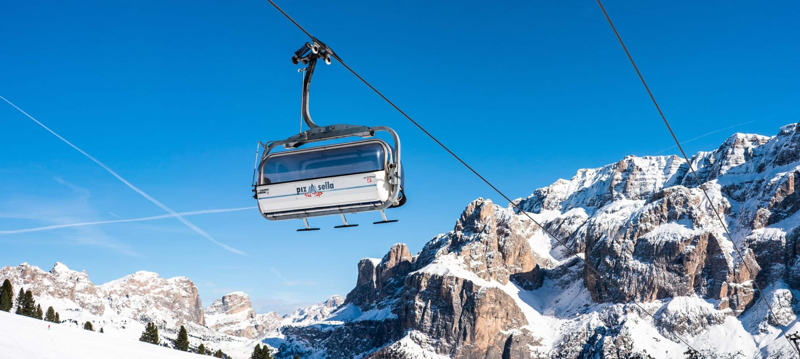 Cabina di seggiovia sospesa su cavo sopra pendii e vette rocciose innevate, cielo blu