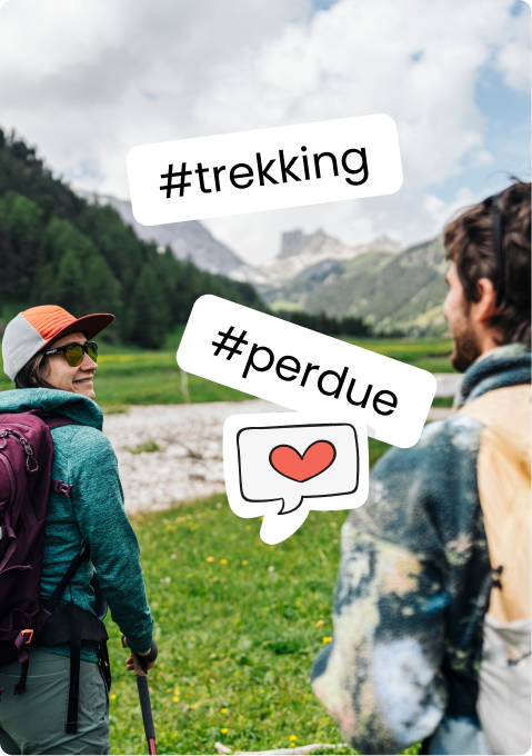 Due escursionisti con zaini in un prato montano, montagne sullo sfondo; sticker #trekking, #perdue e un cuore.