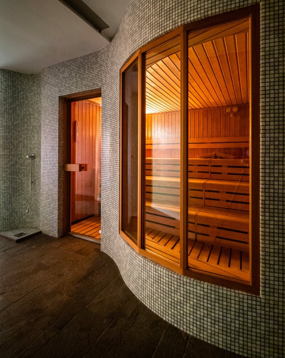 Sauna interna in legno visibile attraverso ampie vetrate, corridoio con parete curva rivestita in piastrelle