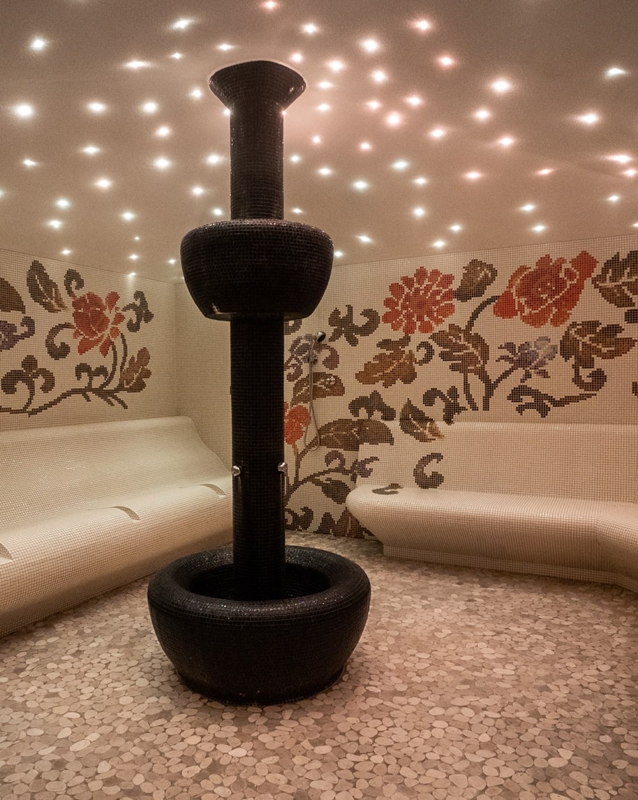 Fontana nera centrale in sala mosaico con panche curve bianche, pareti floreali e soffitto con luci a stelle