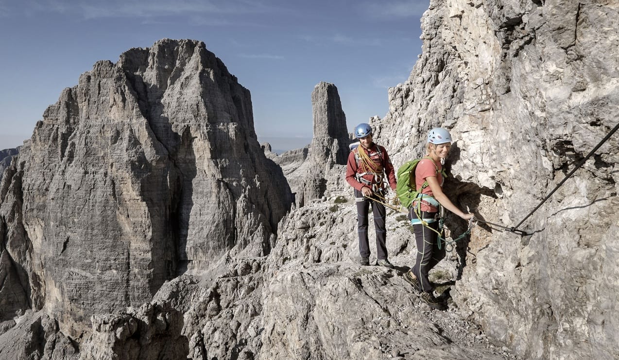 Due alpinisti con caschi e imbragature agganciati a una via ferrata su cresta rocciosa in alta montagna