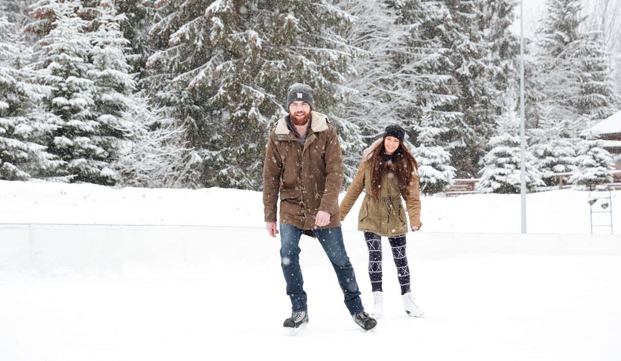 Uomo e donna su pista di ghiaccio all'aperto sotto la neve, lui davanti, lei che lo segue sorridente