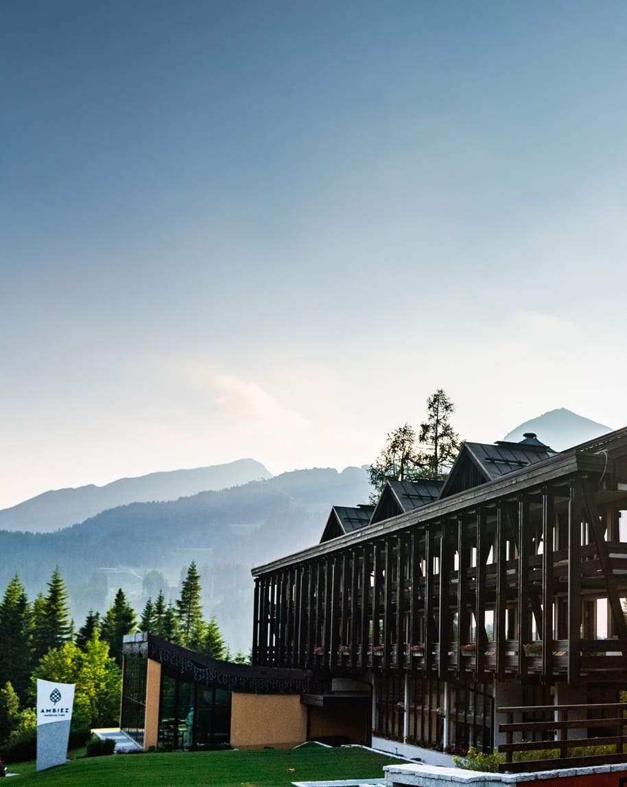 Edificio dell'Hotel Ambiez con portico in legno, prato e montagne sullo sfondo