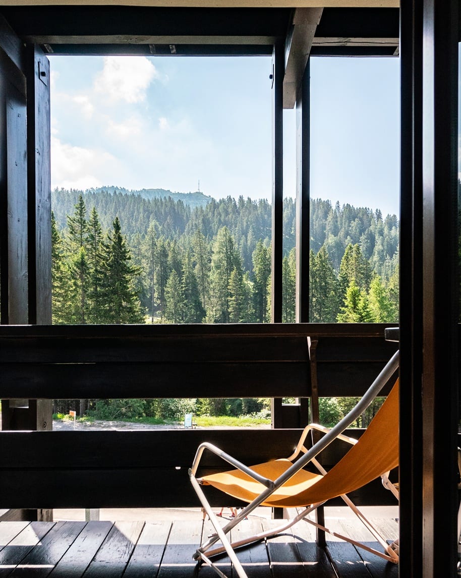 Balcone con sedia pieghevole arancione affacciato su una foresta di conifere e colline sullo sfondo