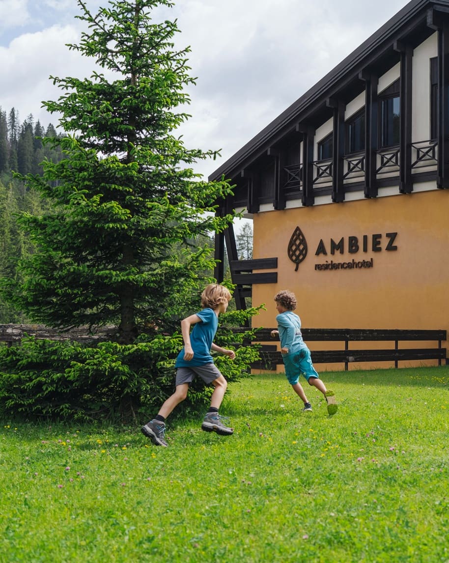 Due bambini che corrono su prato davanti all'edificio Ambiez Residencehotel.