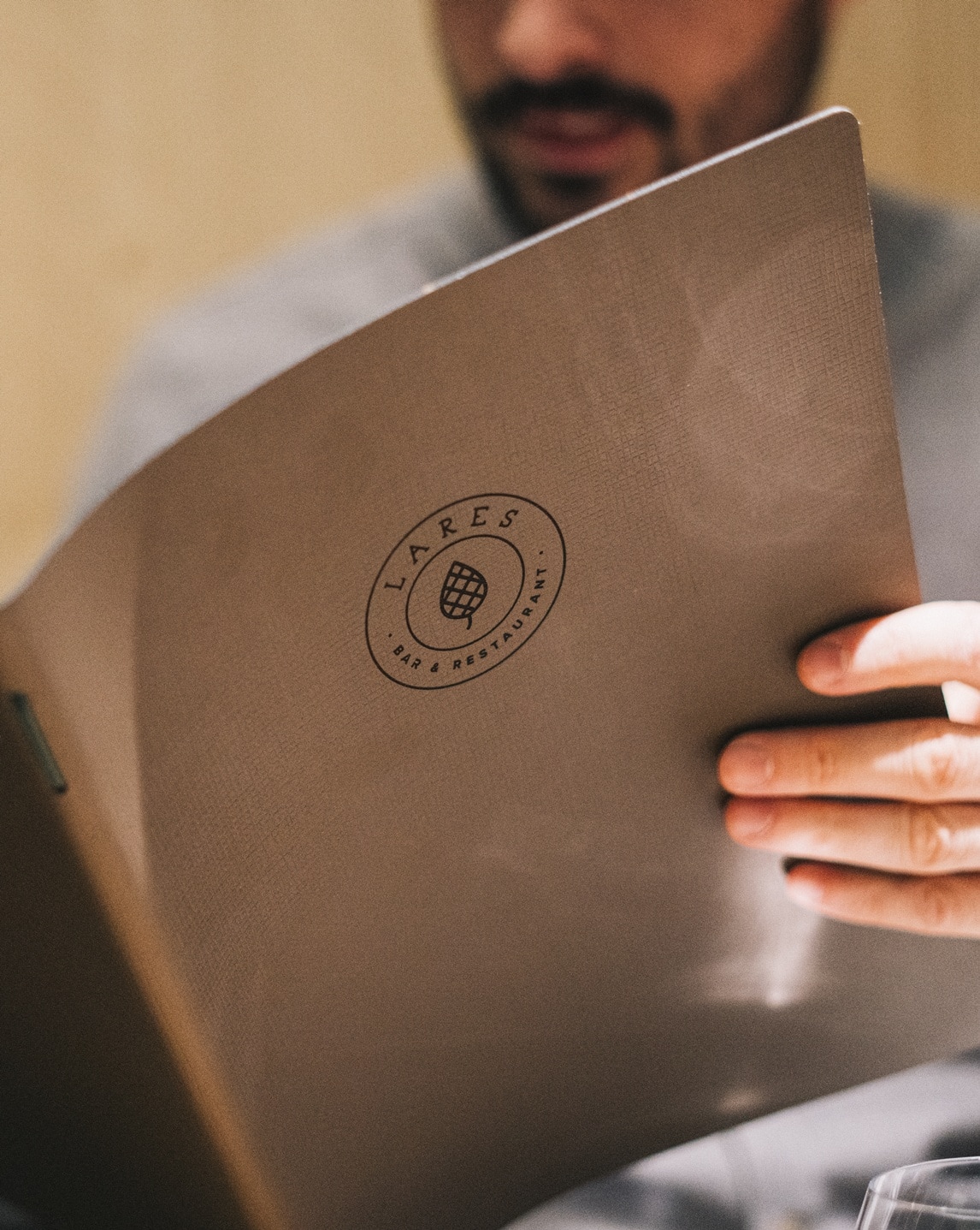 Uomo parzialmente visibile che sfoglia un menu marrone con logo circolare, mano destra sul bordo