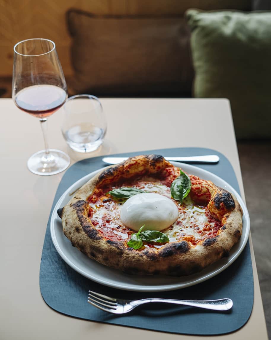 Pizza con burrata al centro e foglie di basilico, su piatto con forchetta e bicchiere di vino