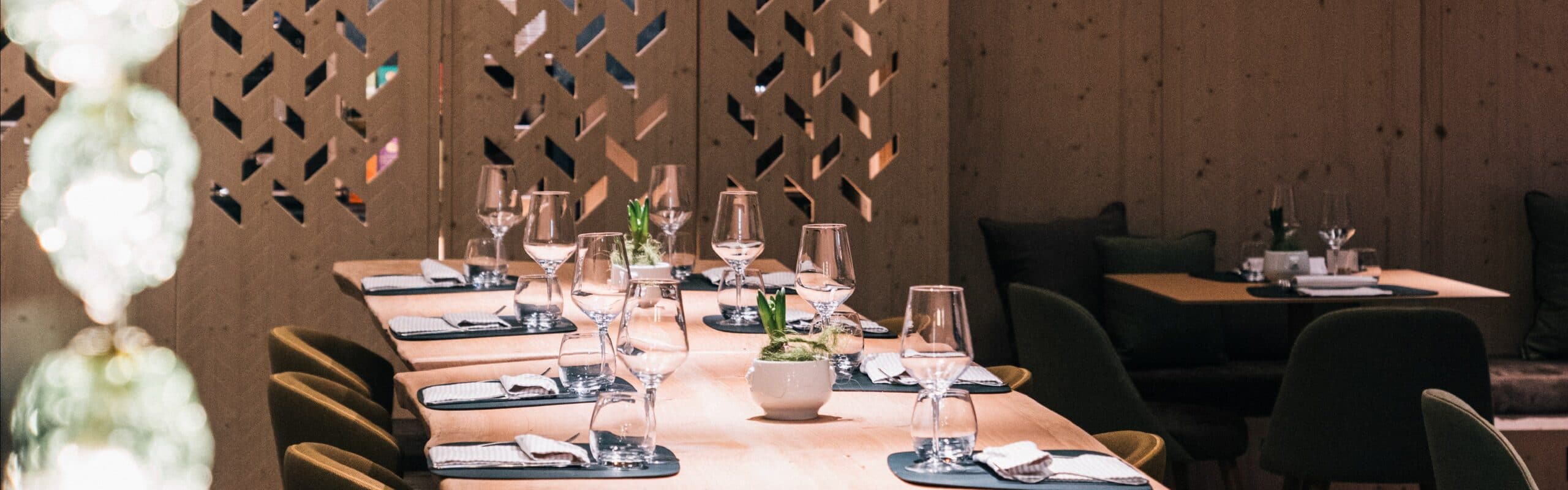 Tavoli apparecchiati in ristorante con calici, bicchieri e piccoli vasi di pianta, pareti e separé in legno