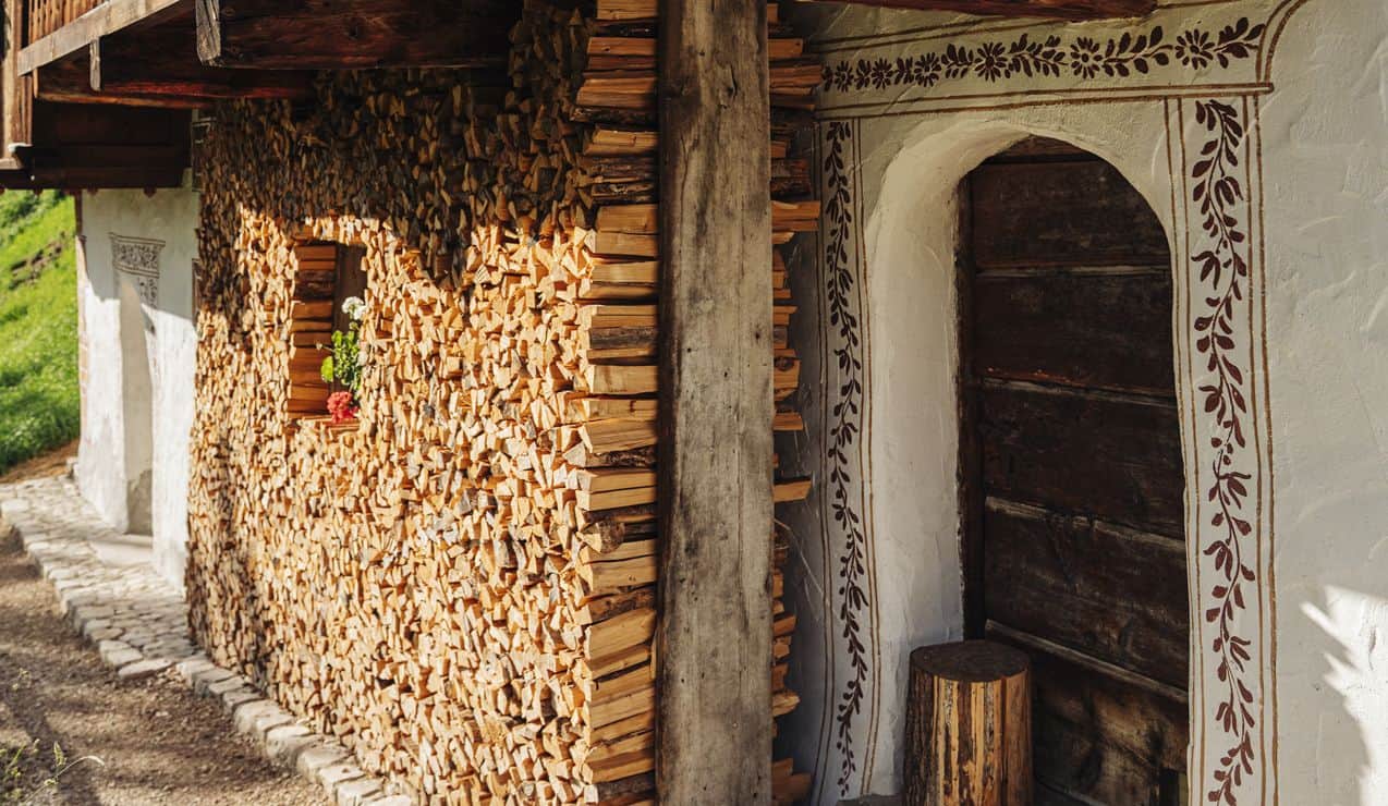 Facciata con legna accatastata, finestrella con fiori e porta in legno con cornice dipinta