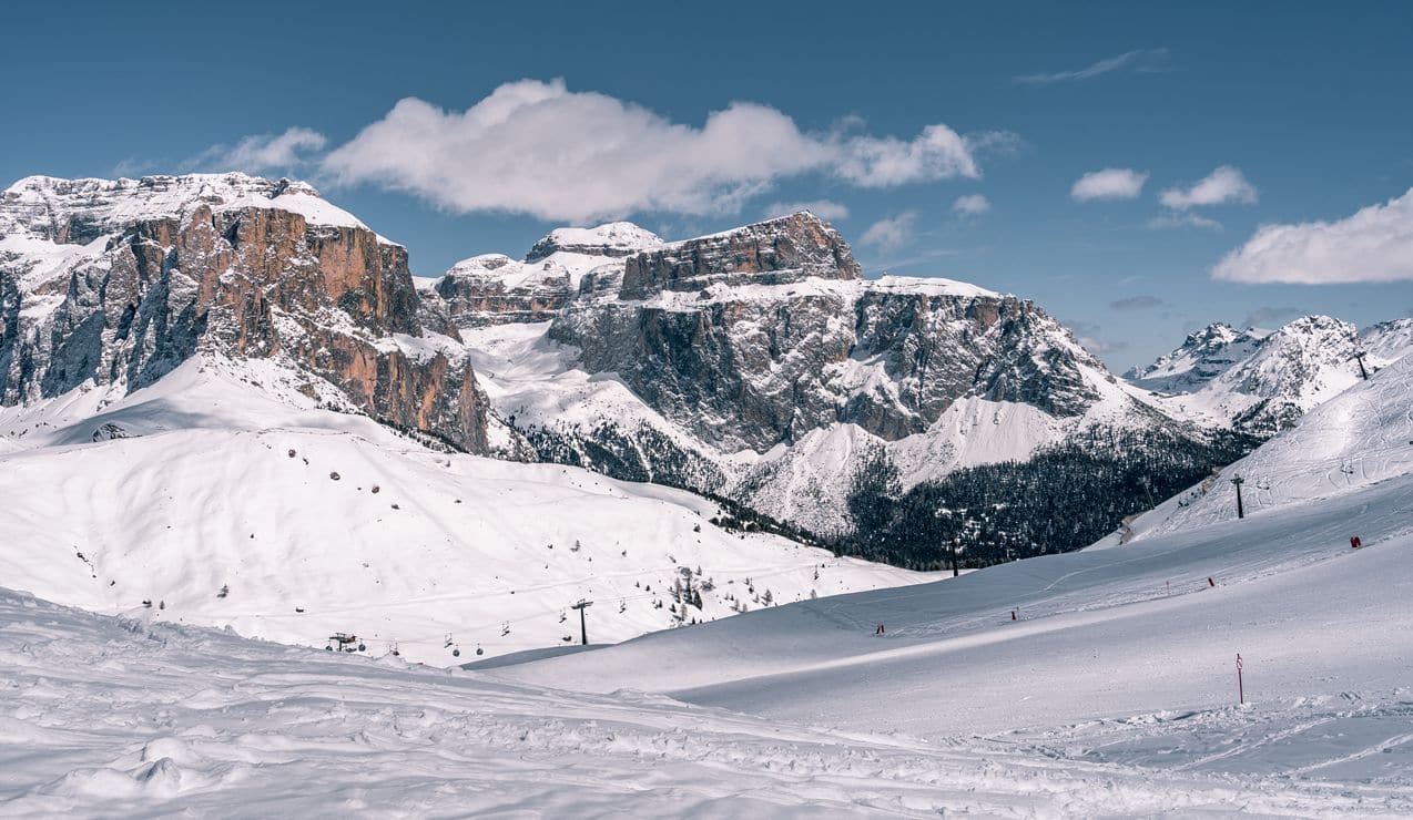 Montagne con pareti rocciose innevate, ampie piste da sci e impianto di risalita