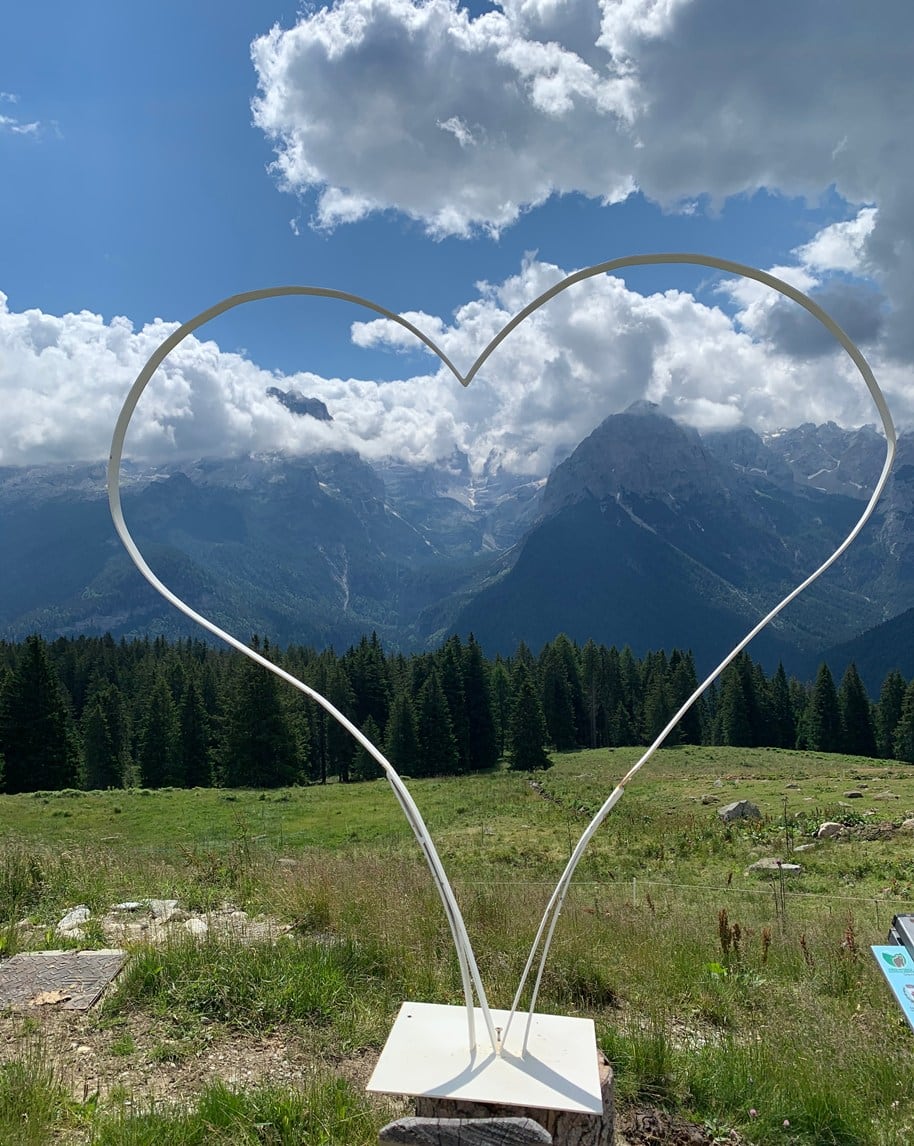 Cornice a forma di cuore in metallo davanti a montagna, foresta e prato sotto nuvole