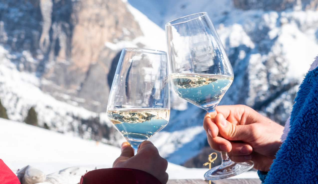 Due calici di vino bianco a un brindisi, mani che li tengono, montagna innevata sullo sfondo