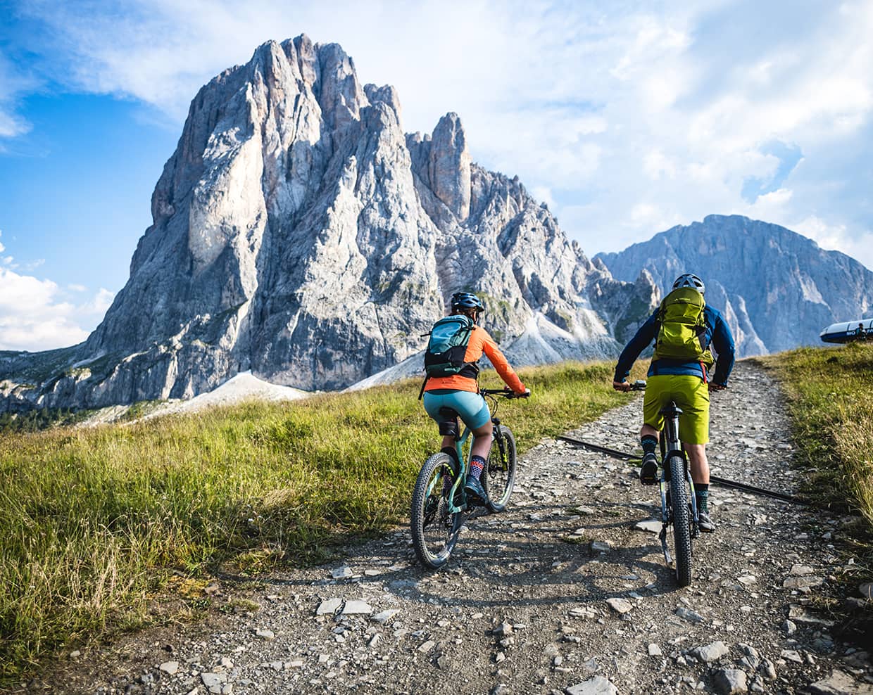 Due ciclisti in mountain bike risalgono un sentiero roccioso verso una parete montuosa