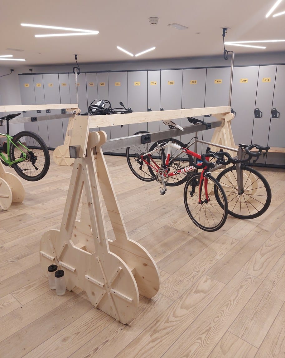 Locale con rastrelliere in legno e biciclette sospese, armadietti grigi numerati sullo sfondo