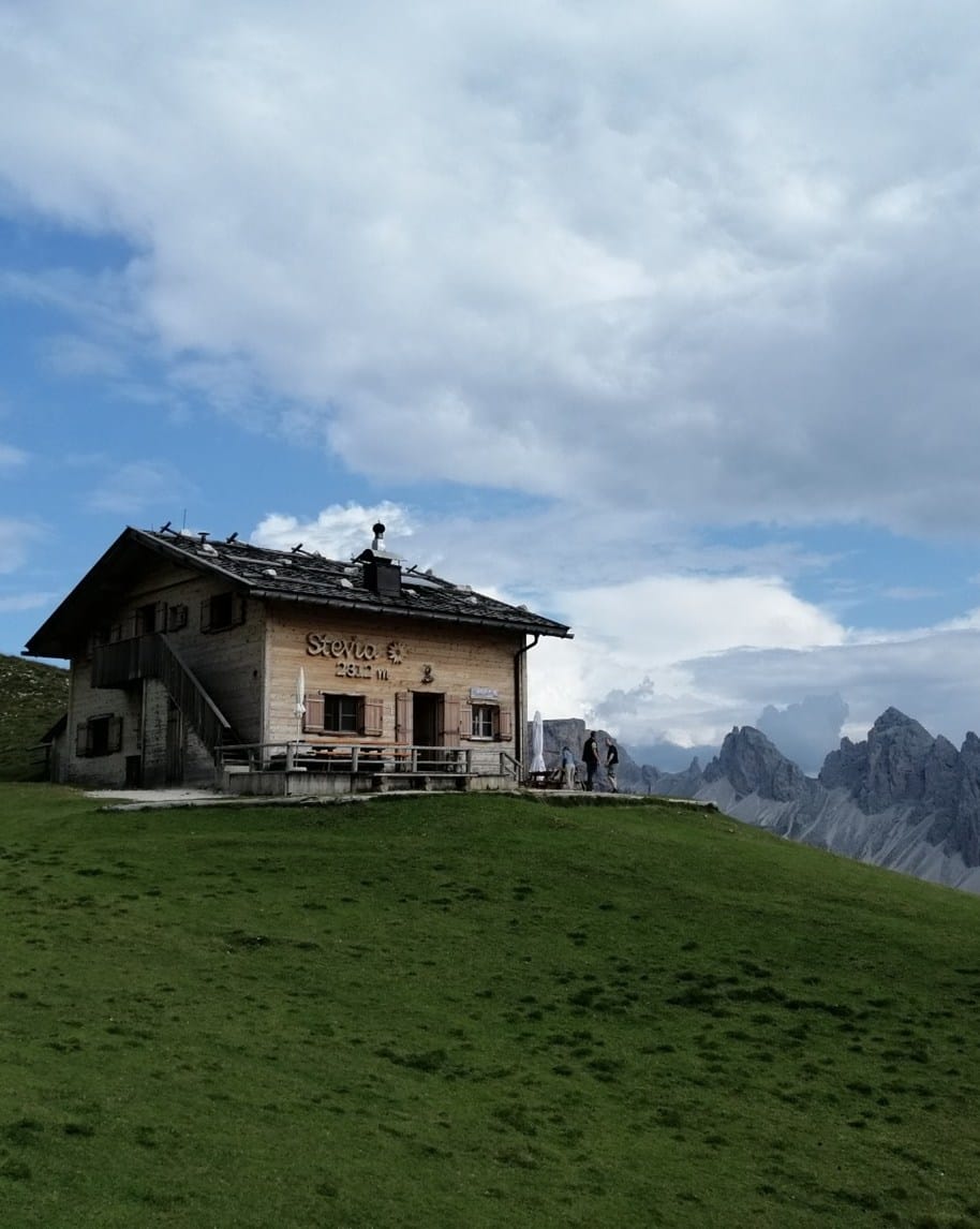 Rifugio Stevia 2311 m su collina erbosa, persone sul terrazzo e montagne rocciose sullo sfondo