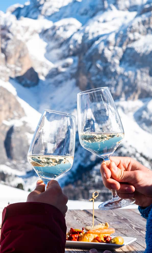 Due calici di vino bianco sollevati in brindisi davanti a montagne innevate, piatto su tavolo