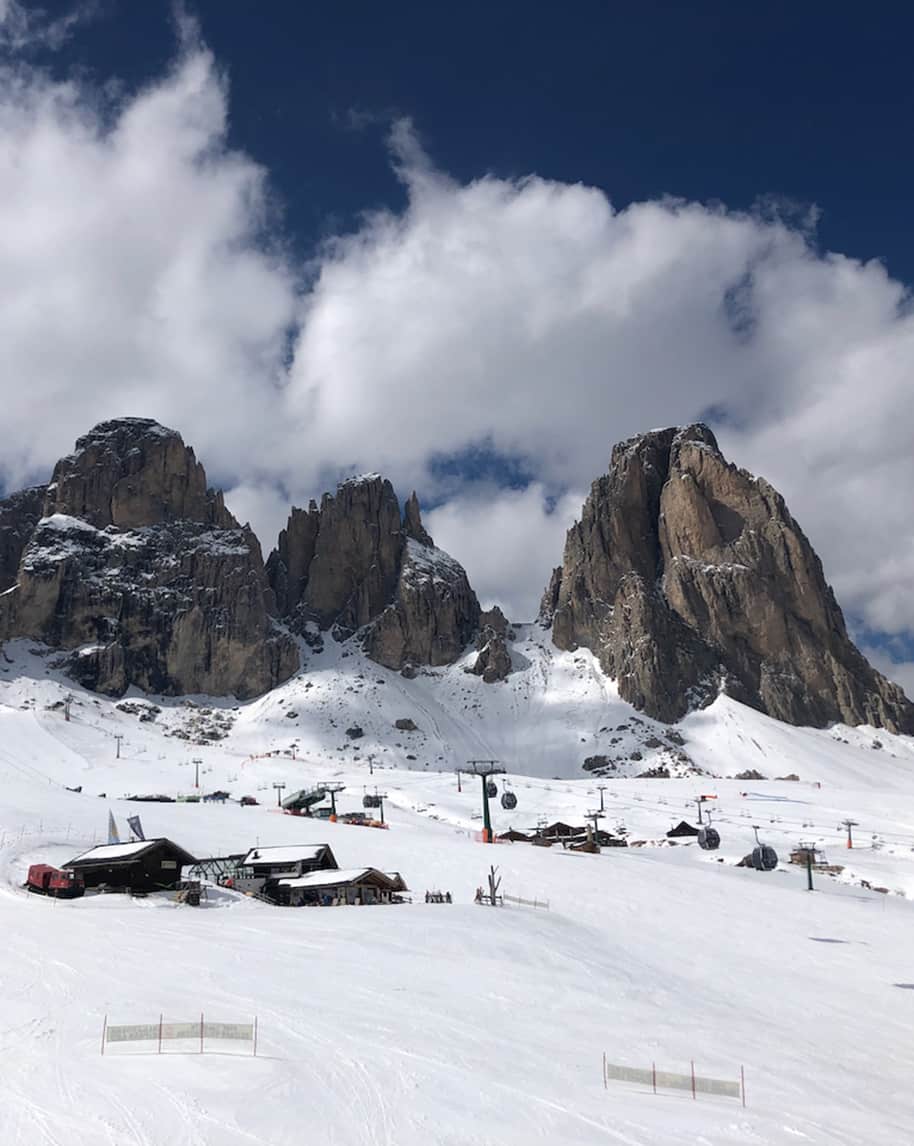 Massiccio roccioso innevato con cabinovie e baite su pendio di neve sotto cielo nuvoloso