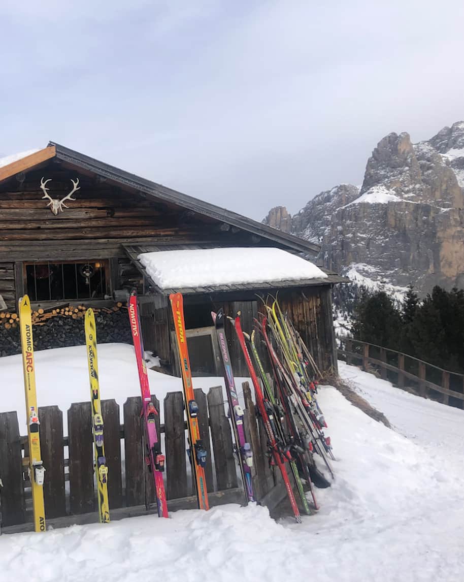 Sci appoggiati a una recinzione di legno davanti a chalet innevato, cime rocciose sullo sfondo