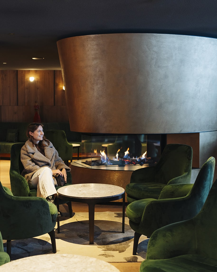 Donna seduta su poltrona verde vicino a camino centrale in vetro in lounge con tavolo tondo