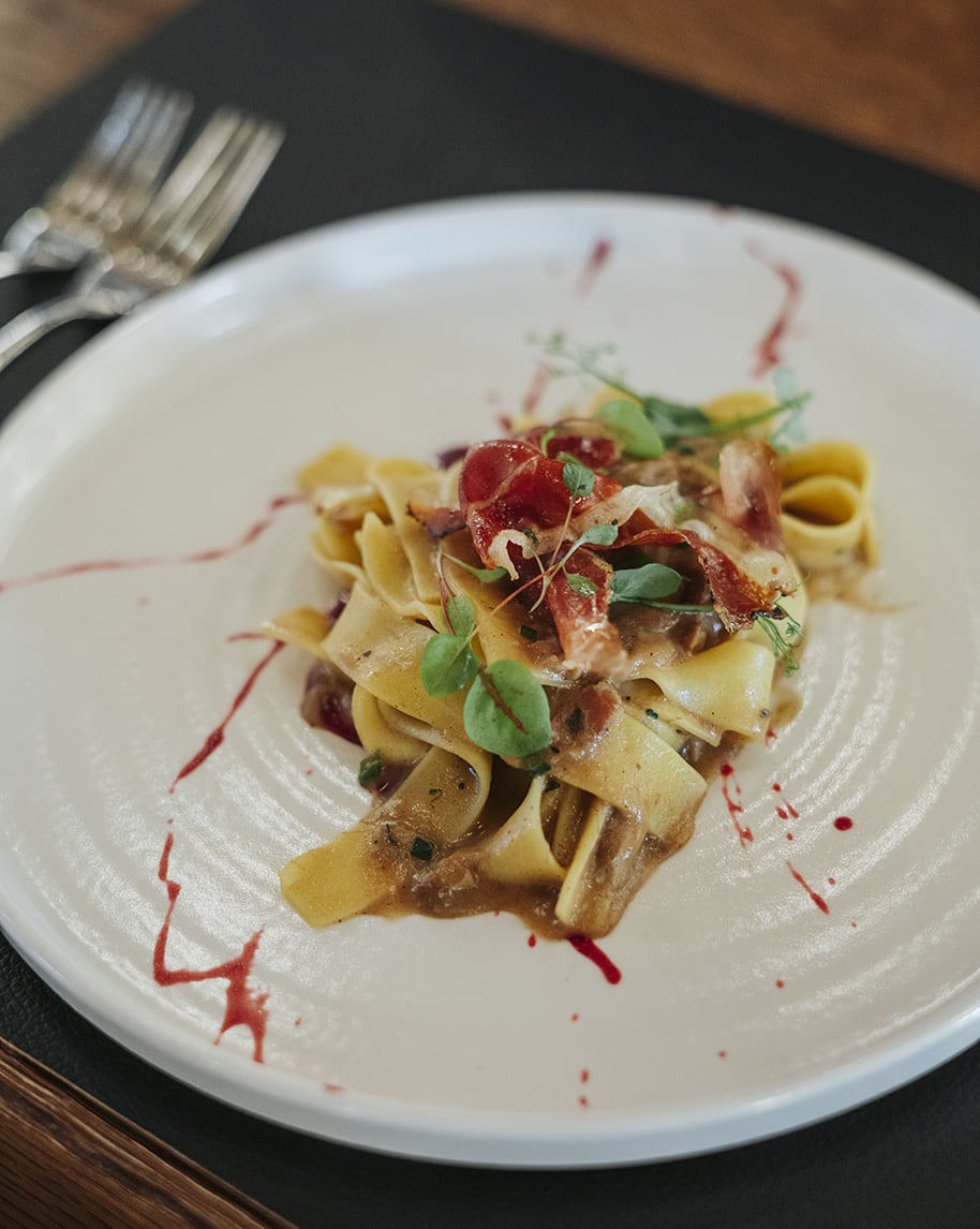 Pasta pappardelle con salsa, scaglie di prosciutto e germogli su piatto bianco con schizzi di salsa rossa