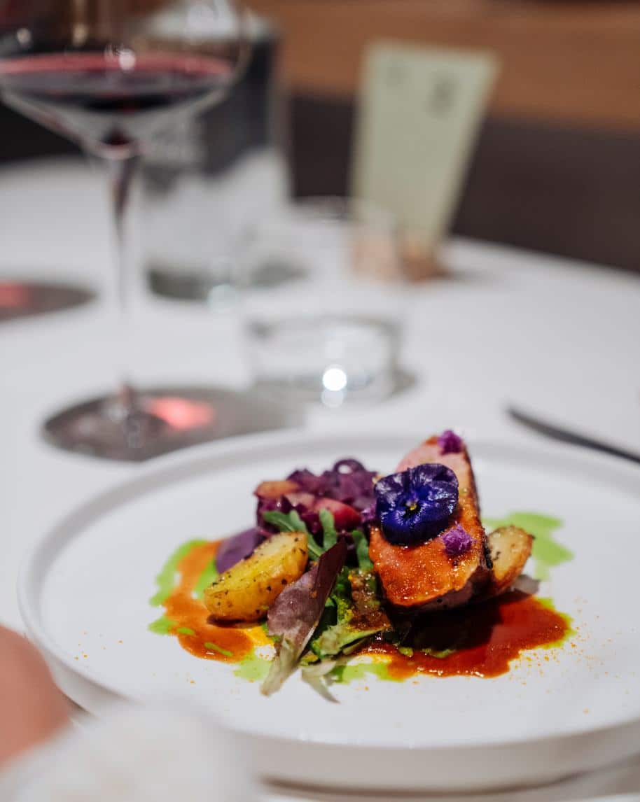 Piatto gourmet con fetta di carne glassata, patate arrostite, insalatina e fiore viola su tavolo apparecchiato