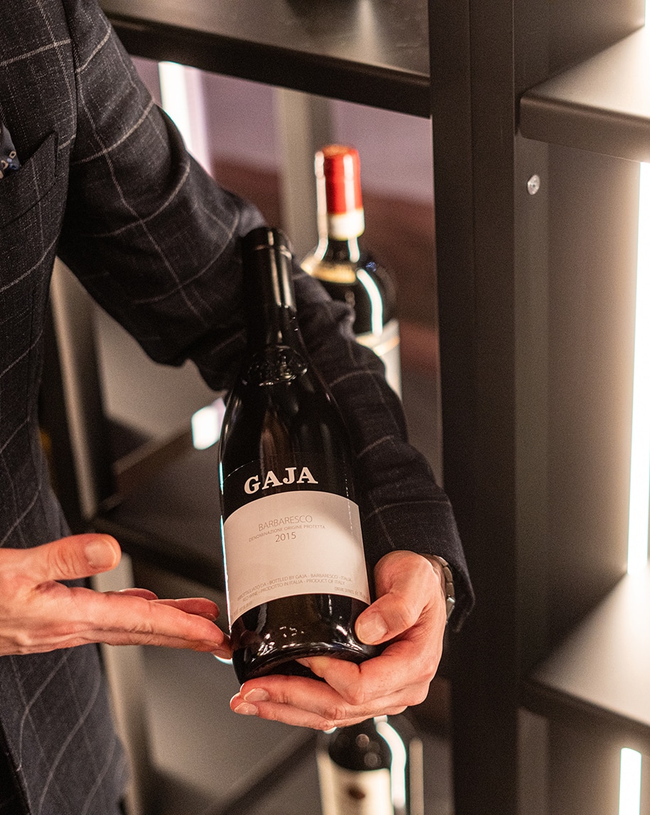 Mani che tengono e mostrano una bottiglia di vino davanti a uno scaffale con altre bottiglie