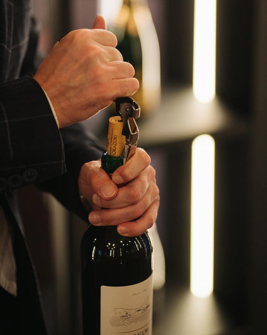Mani che usano un cavatappi per estrarre il tappo da una bottiglia di vino