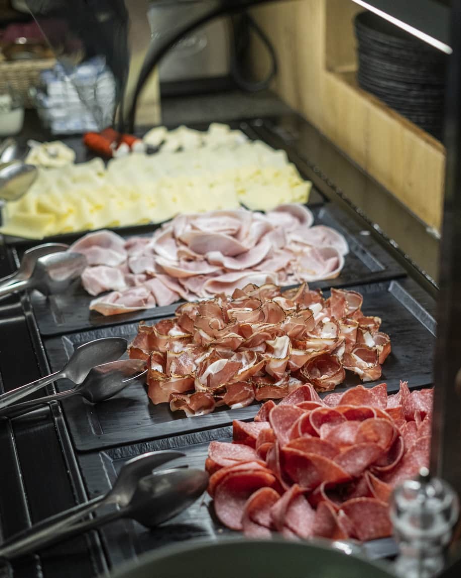 Vassoi da buffet con fette di salumi assortiti e formaggi affettati, con pinze per servizio