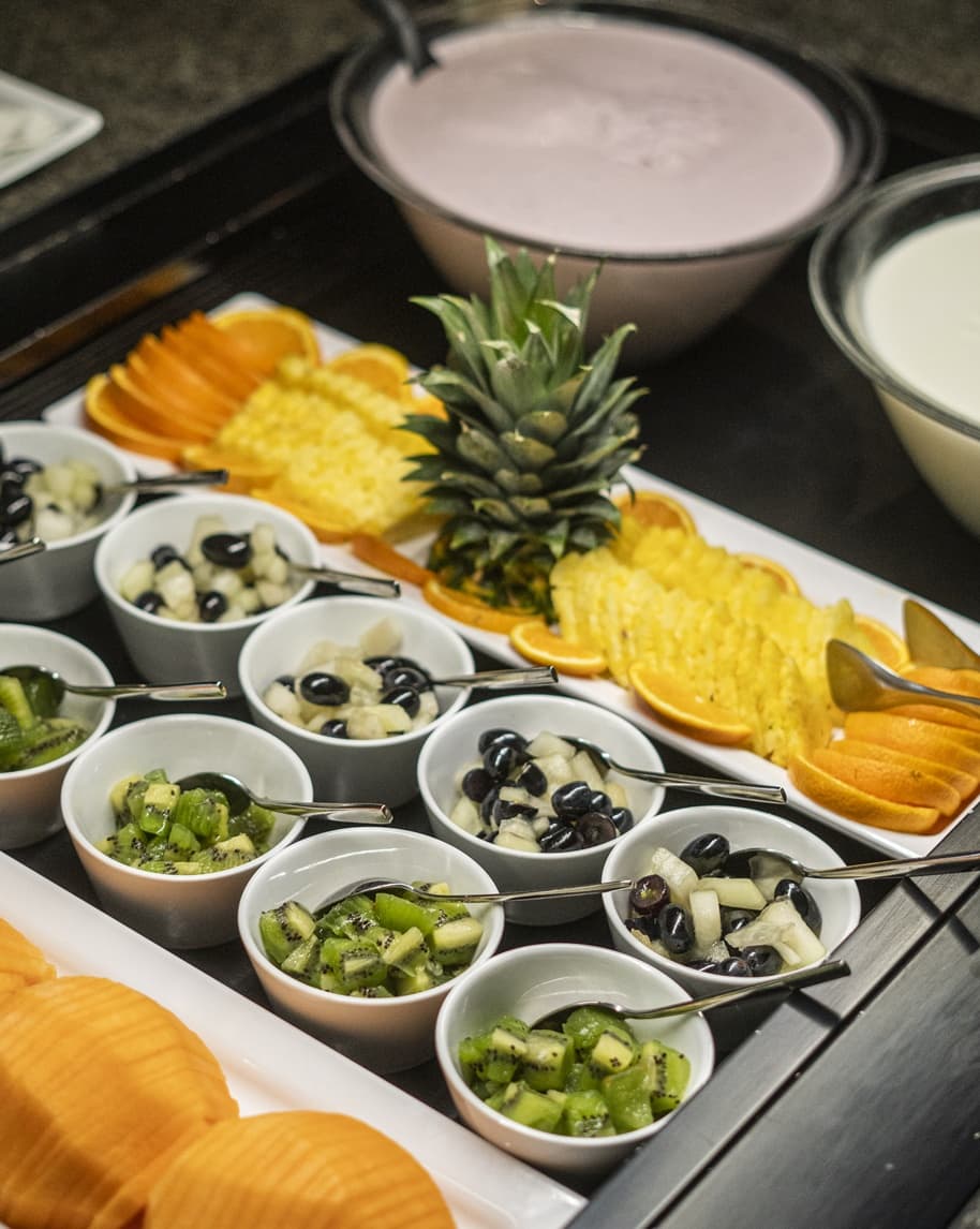 Ciotole con macedonia di kiwi e uva, fette di ananas e arancia con corona di ananas su buffet