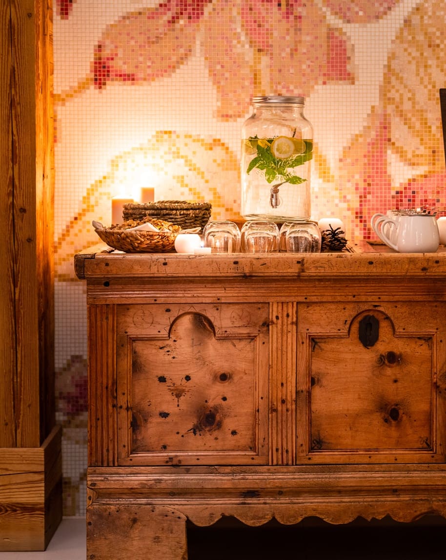 Mobile in legno con dispenser d'acqua (limone e menta), bicchieri, candele e sfondo mosaico