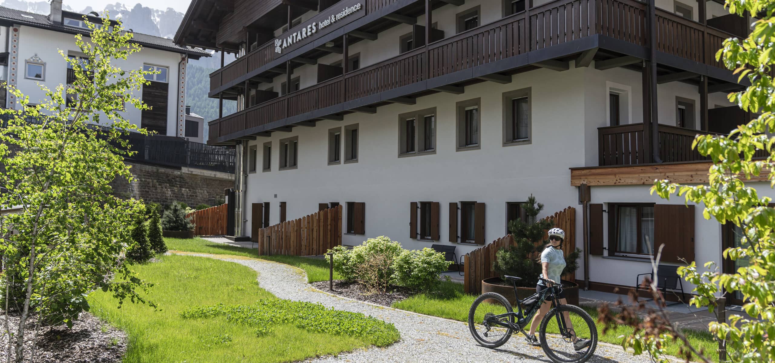 Persona con casco accanto a bicicletta da montagna su sentiero davanti a edificio Antares Hotel & Residence