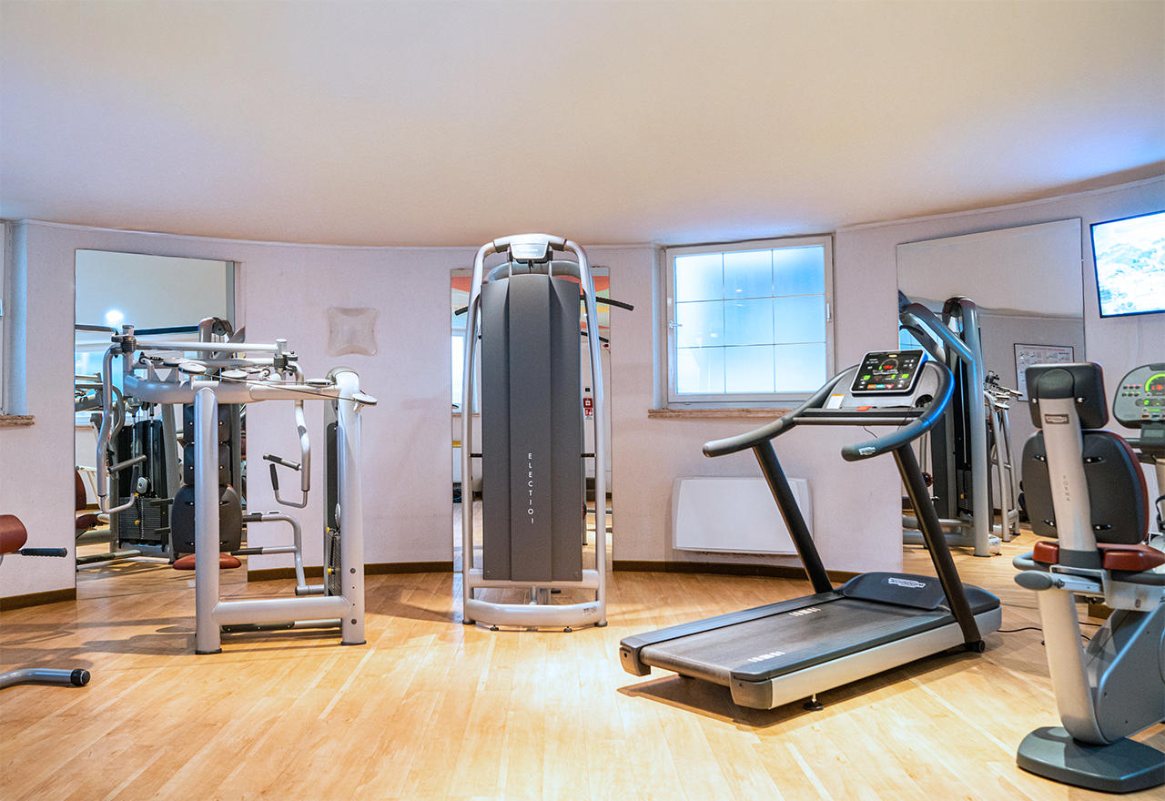 Sala fitness con tapis roulant, macchine multifunzione, pavimento in legno e specchi alle pareti
