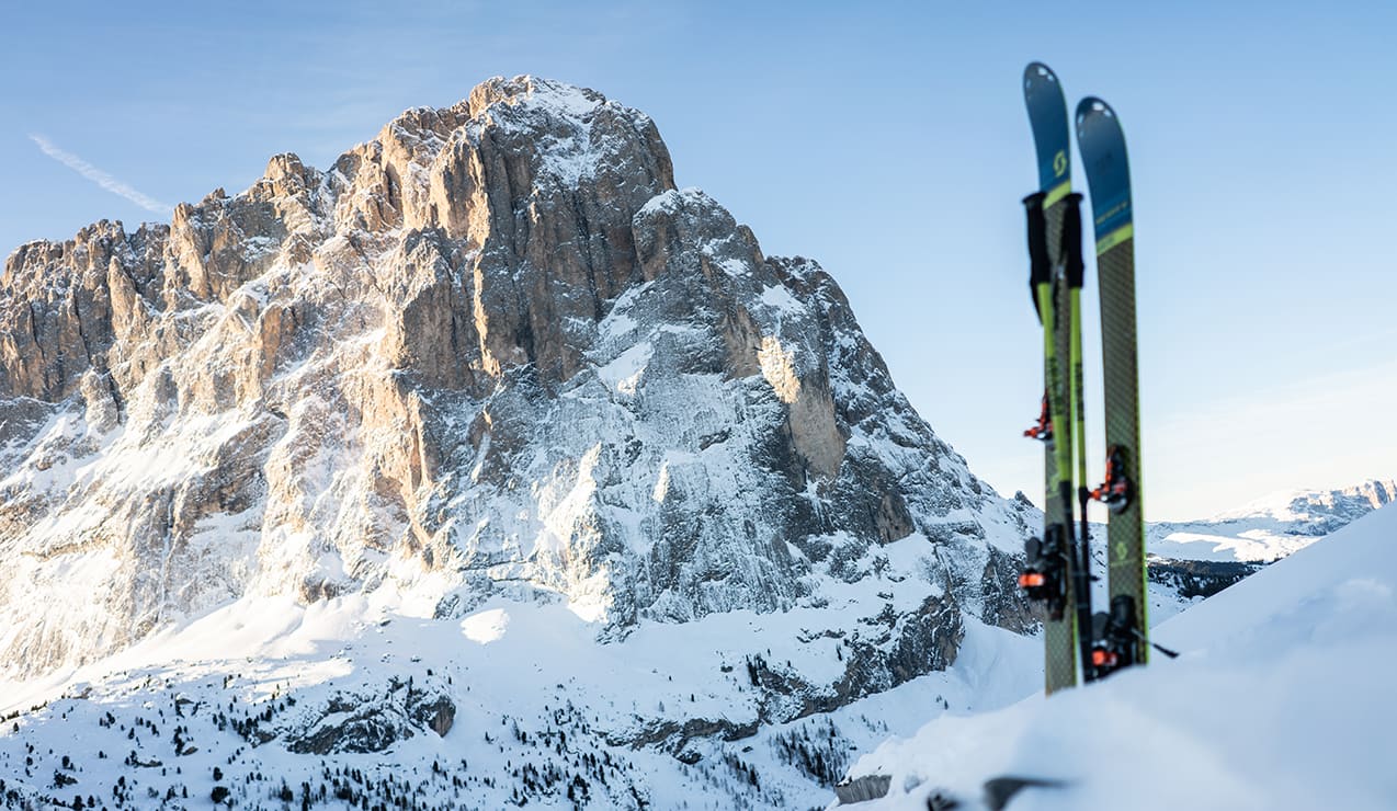Sci piantati nella neve a destra, grande parete rocciosa innevata sullo sfondo
